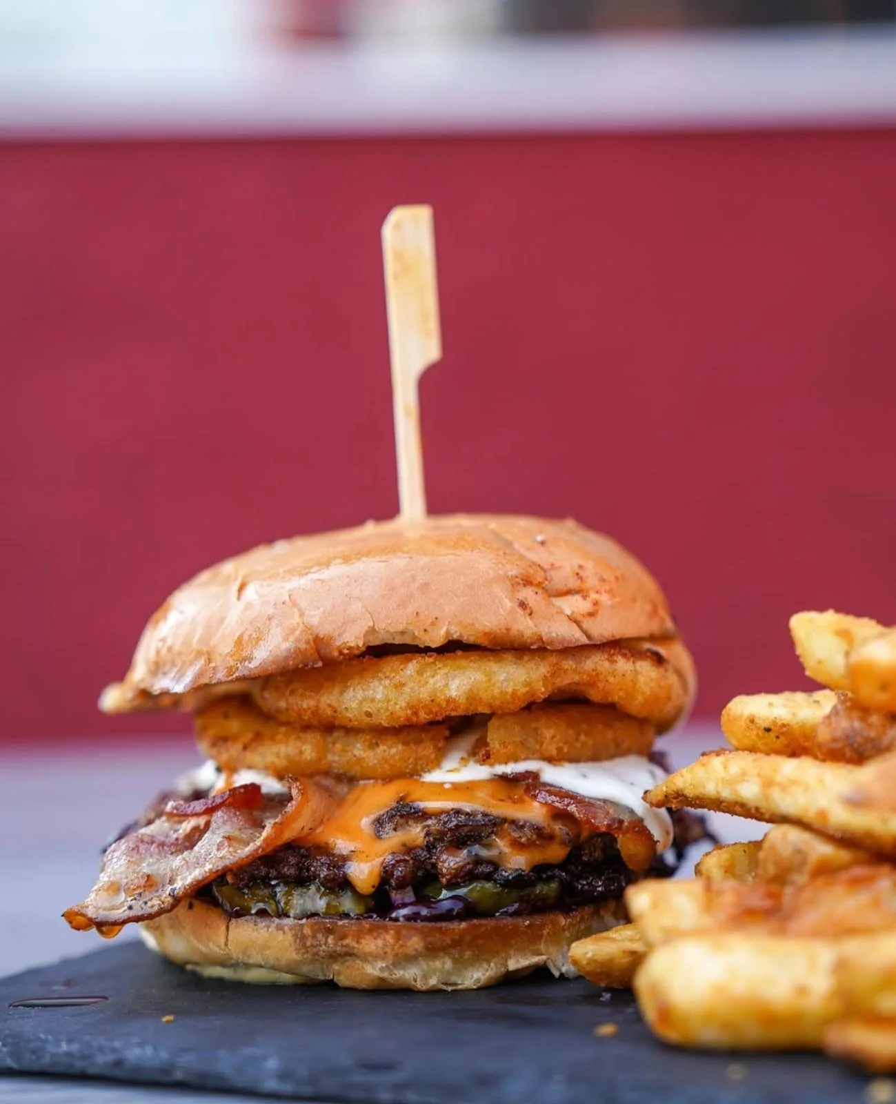 A smash burger stacked with onion rings, bacon and cheddar, with fries