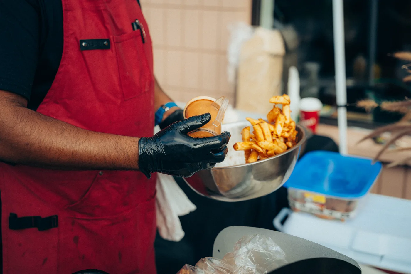 A cook in a red apron holding a smash burger and a basket of fries