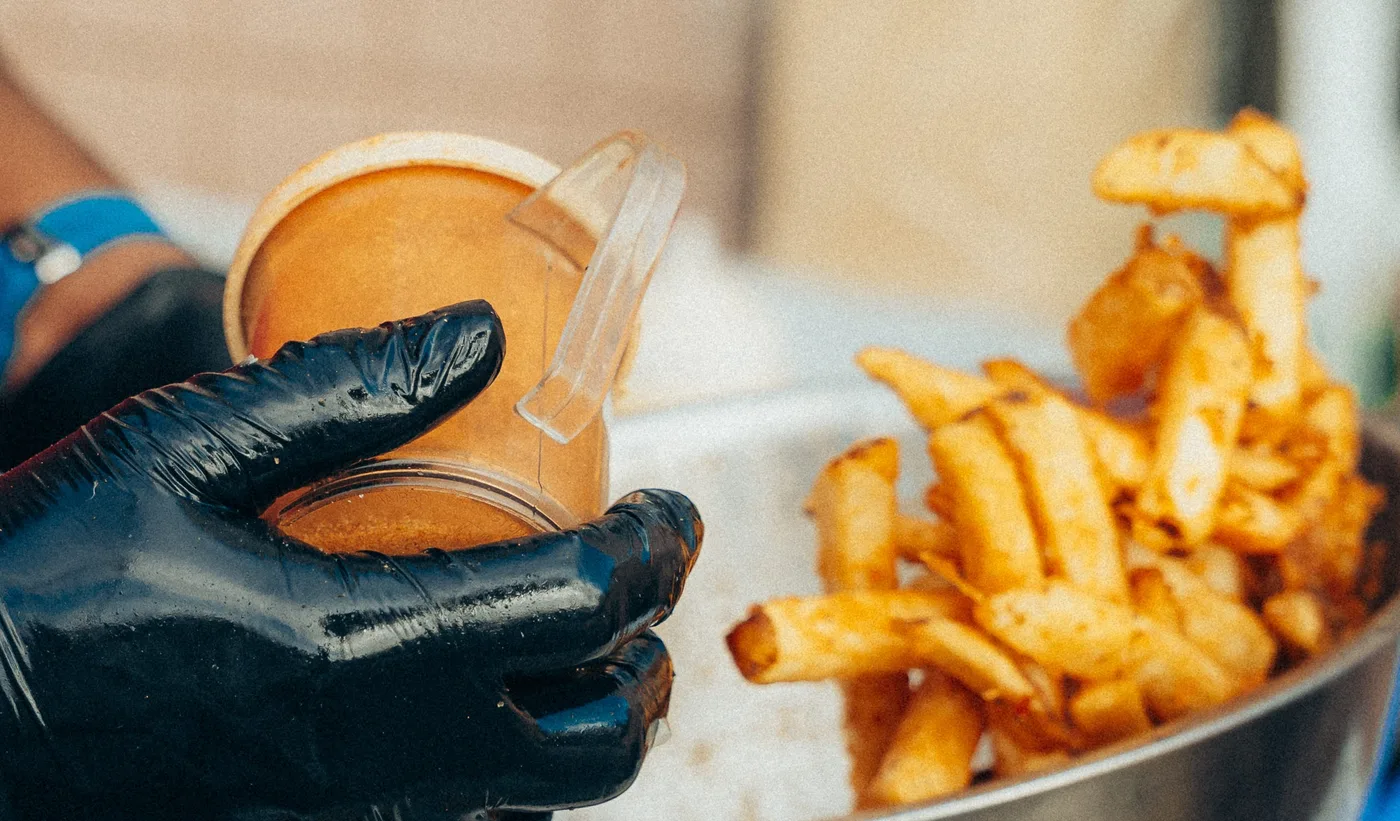 A gloved hand holding a dip cup beside a bowl of seasoned fries