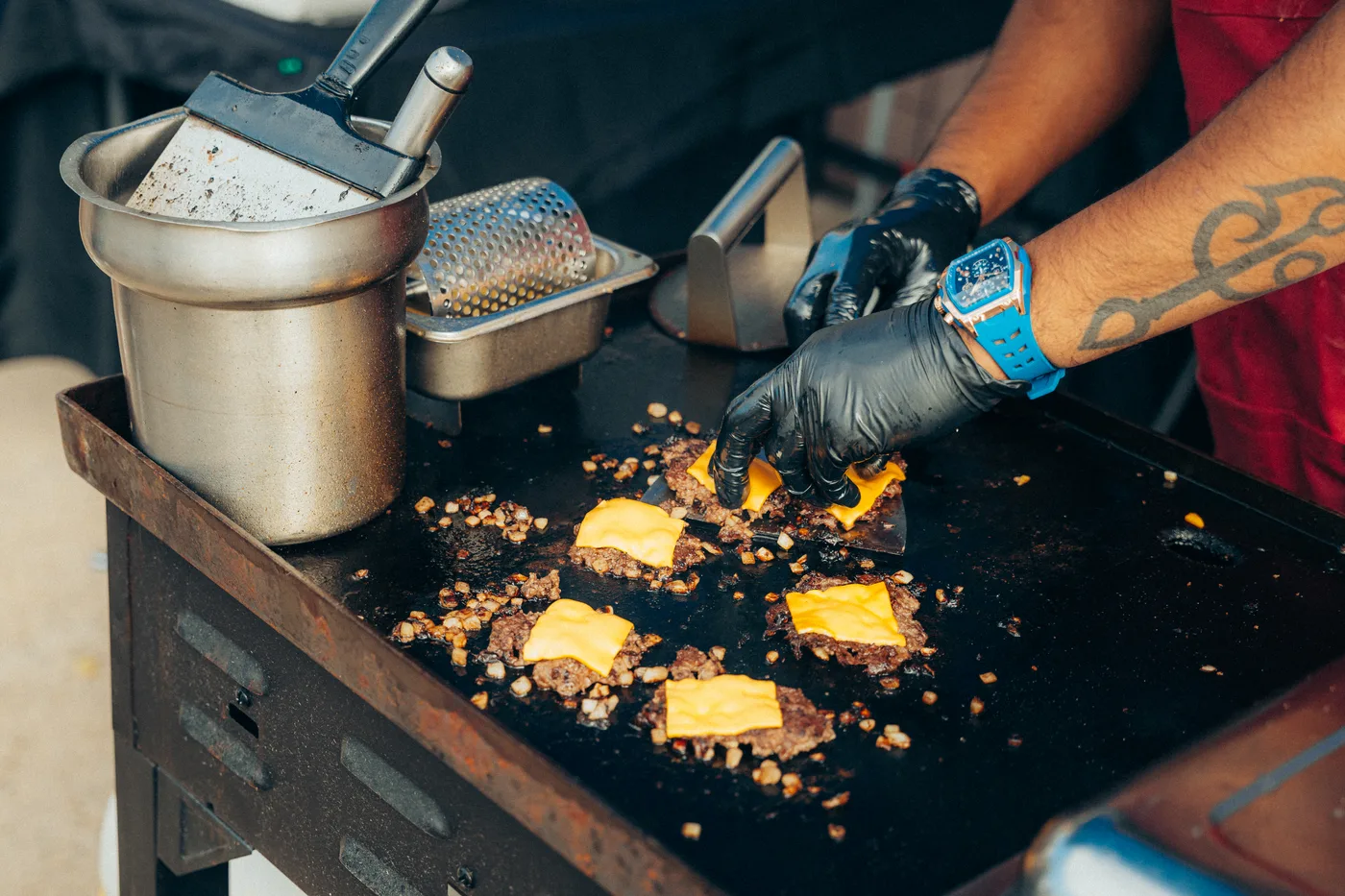 Patties being smashed on a flat-top griddle as the cheese goes on